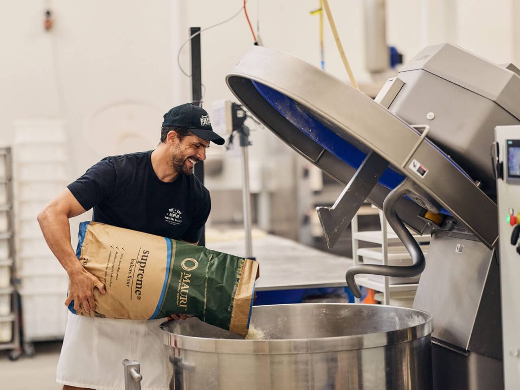 A male baker pouring flour into an industrial moxer