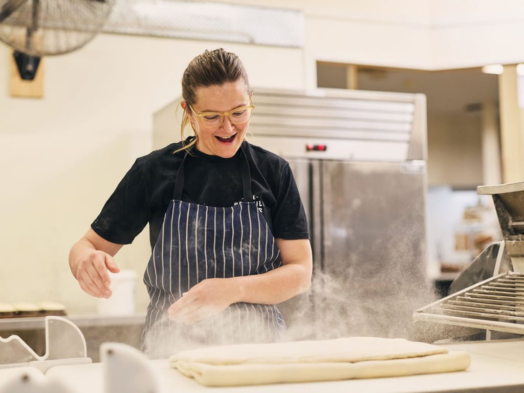 Baker smiling throwing flower over dough