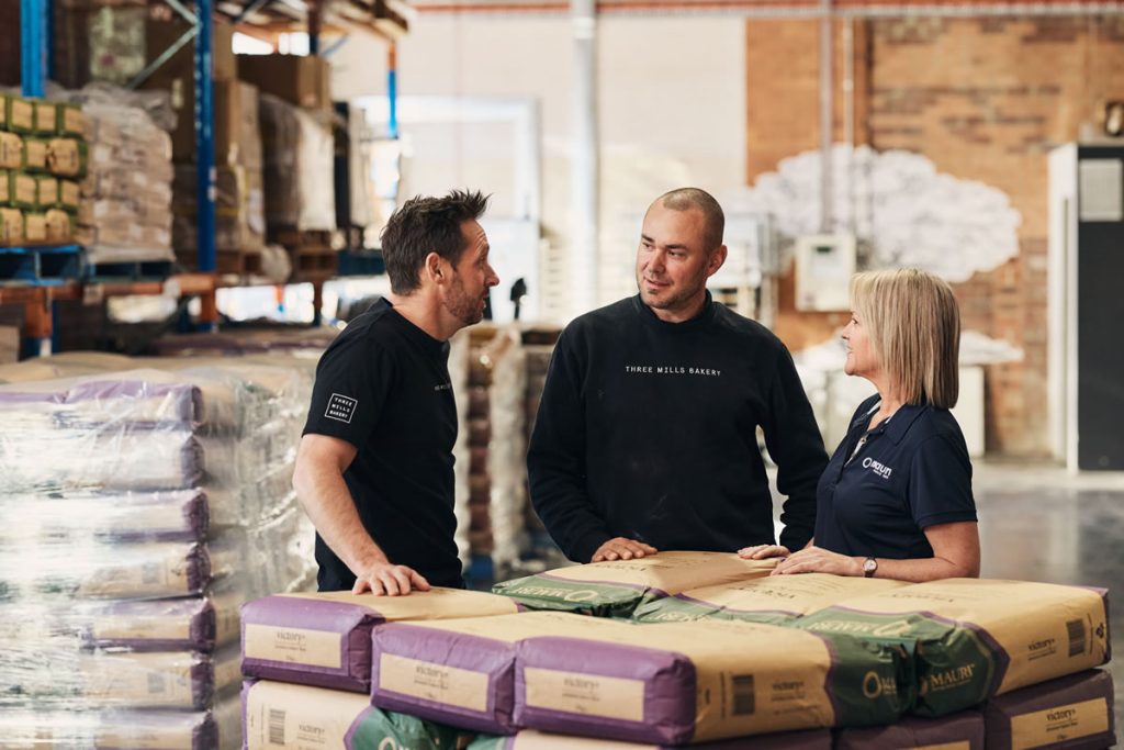 Two men and a woman chatting and smiling in a warehouse