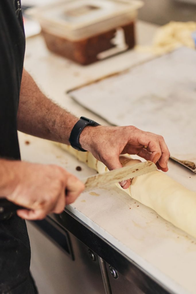 Close up on man holding a knife slicing pastry roll