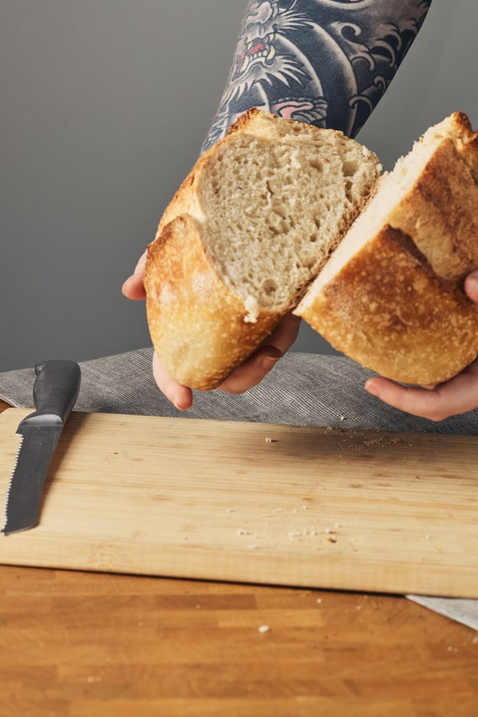 A person holding a cut loaf of bread in two hands showing the inside of the bread