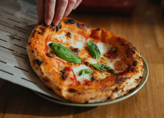A freshly cooked margarita pizza with basil leaves on top being slid onto a plate